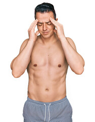 Fototapeta premium Handsome young man wearing swimwear shirtless with hand on head, headache because stress. suffering migraine.