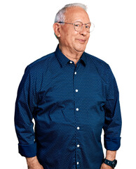 Senior man with grey hair wearing casual shirt and glasses smiling looking to the side and staring away thinking.