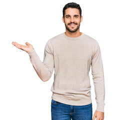 Fototapeta premium Young hispanic man wearing casual clothes smiling cheerful presenting and pointing with palm of hand looking at the camera.
