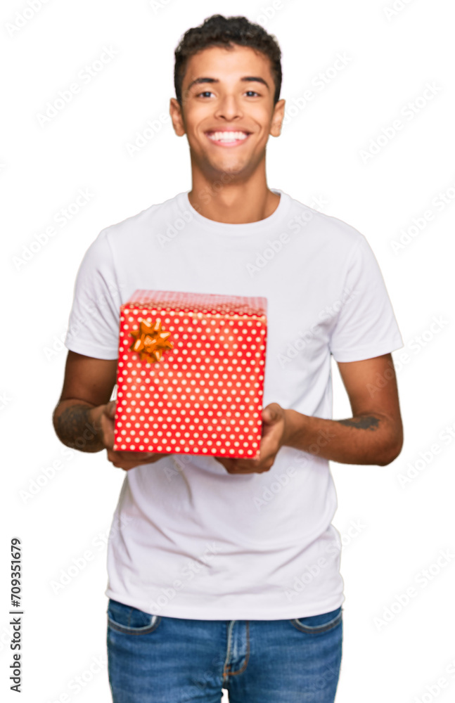 Poster Young handsome african american man holding gift looking positive and happy standing and smiling with a confident smile showing teeth