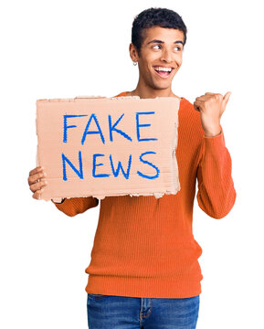 Young african amercian man holding fake news banner pointing thumb up to the side smiling happy with open mouth