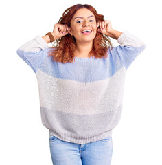 Young latin woman wearing casual clothes smiling pulling ears with fingers, funny gesture. audition...