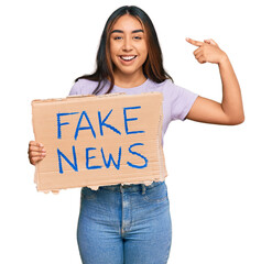 Young latin woman holding fake news banner pointing finger to one self smiling happy and proud