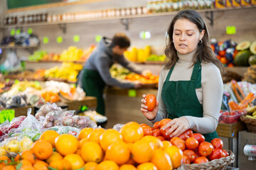 Saleswoman in an apron puts ripe tomatoes on a supermarket window