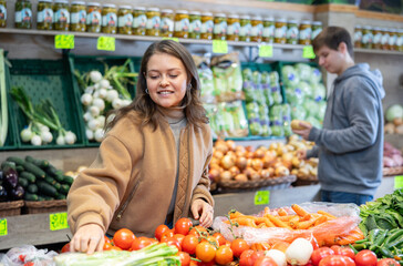 Obraz premium Young female shopper selects and buys tomatoes in a supermarket