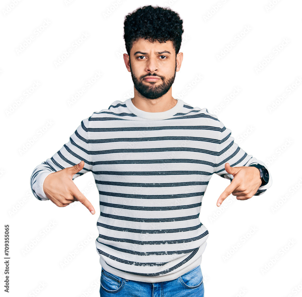 Sticker Young arab man with beard wearing casual striped sweater pointing down looking sad and upset, indicating direction with fingers, unhappy and depressed.