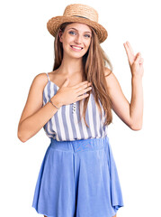 Young beautiful blonde woman wearing summer hat smiling swearing with hand on chest and fingers up,...