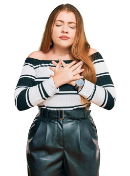 Young beautiful redhead woman wearing elegant clothes smiling with hands on chest with closed eyes and grateful gesture on face. health concept.
