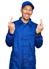 Bald man with beard wearing builder jumpsuit uniform showing middle finger doing fuck you bad expression, provocation and rude attitude. screaming excited