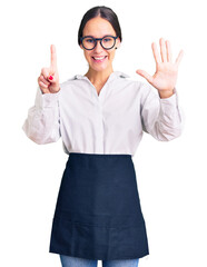 Beautiful brunette young woman wearing professional waitress apron showing and pointing up with fingers number six while smiling confident and happy.