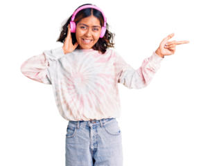 Young beautiful mixed race woman listening to music using headphones smiling happy pointing with hand and finger to the side
