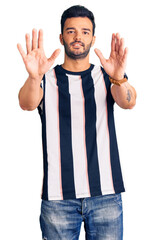 Fototapeta premium Young handsome hispanic man wearing striped tshirt afraid and terrified with fear expression stop gesture with hands, shouting in shock. panic concept.