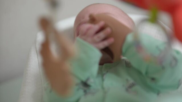 Infant baby boy lying on bed while playing teether. A baby scratches his gums chewing teething toy.