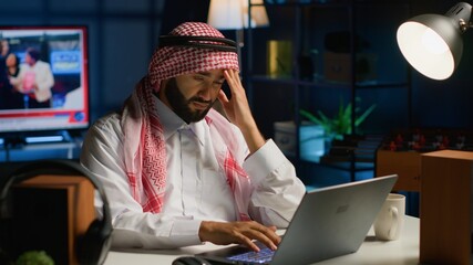 Tired arab businessman suffering migraine working from home office. Exhausted Middle Eastern worker...