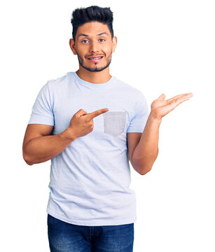 Handsome latin american young man wearing casual clothes amazed and smiling to the camera while presenting with hand and pointing with finger.