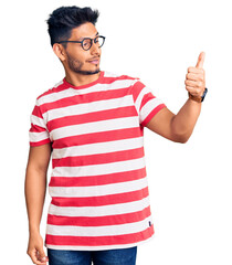 Handsome latin american young man wearing casual clothes and glasses looking proud, smiling doing thumbs up gesture to the side