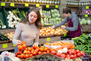 Young female shopper selects and buys tomatoes in a supermarket