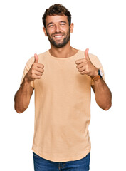 Handsome young man with beard wearing casual tshirt success sign doing positive gesture with hand, thumbs up smiling and happy. cheerful expression and winner gesture.