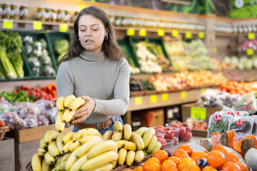 Delighted girl purchaser choosing bananas at the counter in large grocery store