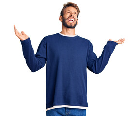 Handsome blond man with beard wearing casual sweater crazy and mad shouting and yelling with aggressive expression and arms raised. frustration concept.