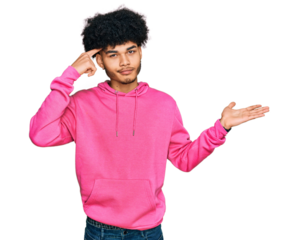 Young african american man with afro hair wearing casual pink sweatshirt confused and annoyed with open palm showing copy space and pointing finger to forehead. think about it.
