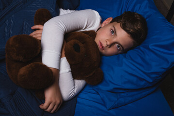 Young boy lying awake in bed clutching his teddy bear