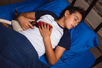 Young boy in bed sleeping with his stuffed animal toy - obrazy, fototapety, plakaty