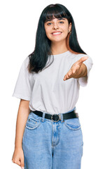 Young hispanic girl wearing casual clothes smiling friendly offering handshake as greeting and welcoming. successful business.