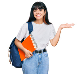 Young hispanic girl wearing student backpack and holding book celebrating victory with happy smile...