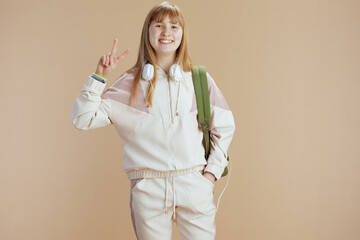 smiling trendy woman in beige tracksuit showing victory