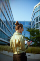modern female employee near office building using smartphone