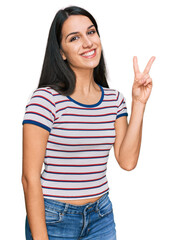 Young hispanic girl wearing casual striped t shirt showing and pointing up with fingers number two while smiling confident and happy.