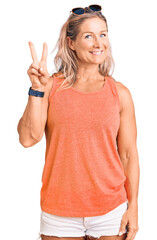 Middle age fit blonde woman wearing casual summer clothes and sunglasses showing and pointing up with fingers number two while smiling confident and happy.