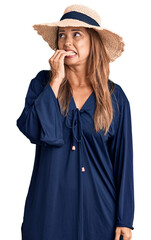 Fototapeta premium Middle age hispanic woman wearing summer hat looking stressed and nervous with hands on mouth biting nails. anxiety problem.