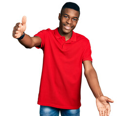 Fototapeta premium Young african american man wearing casual red t shirt looking at the camera smiling with open arms for hug. cheerful expression embracing happiness.