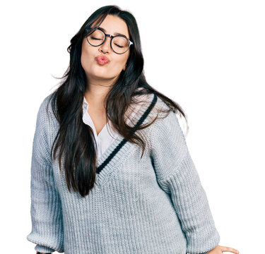 Beautiful hispanic woman wearing casual sweater and glasses looking at the camera blowing a kiss on air being lovely and sexy. love expression.