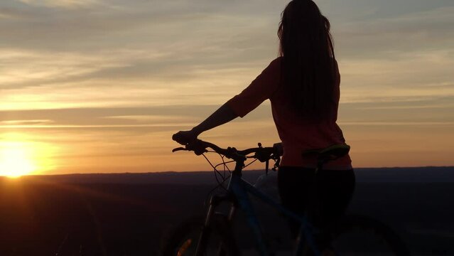 Silhouette of woman cyclist with a bicycle during a sunset high in the mountain