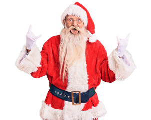 Old senior man with grey hair and long beard wearing traditional santa claus costume shouting with crazy expression doing rock symbol with hands up. music star. heavy music concept.