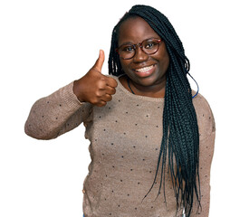 Young black woman with braids wearing casual clothes and glasses smiling happy and positive, thumb...