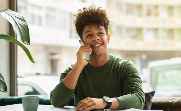 Smiling african american guy sitting at cafe, talking on phone