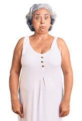 Senior woman with gray hair wearing casual clothes puffing cheeks with funny face. mouth inflated with air, crazy expression.