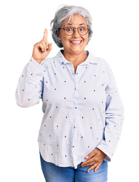 Senior woman with gray hair wearing casual business clothes and glasses pointing finger up with successful idea. exited and happy. number one.