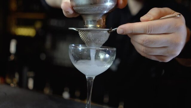 The bartender behind the bar makes an alcoholic cocktail using a glass and a shaker, a very beautiful cocktail in a nightclub, expensive alcohol in a glass in an expensive restaurant