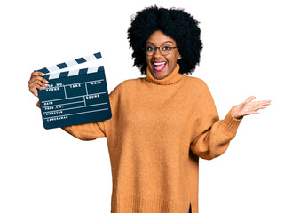 Young african american woman holding video film clapboard celebrating achievement with happy smile...