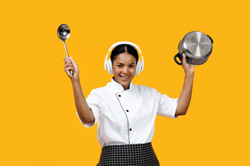 Black female chef enjoying music in headphones while holding ladle and pot
