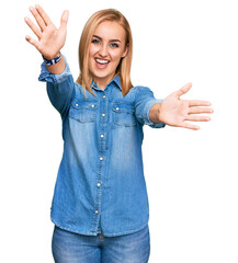 Beautiful caucasian woman wearing casual denim jacket looking at the camera smiling with open arms for hug. cheerful expression embracing happiness.