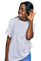 Young african american woman wearing casual white t shirt smiling with hand over ear listening an hearing to rumor or gossip. deafness concept.