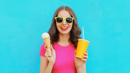 Summer portrait of happy smiling young woman eating ice cream and holding cup of fresh juice wearing sunglasses on blue background