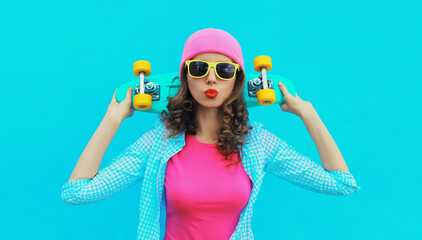 Portrait of stylish modern young woman with skateboard posing in colorful vivid clothes, pink hat...
