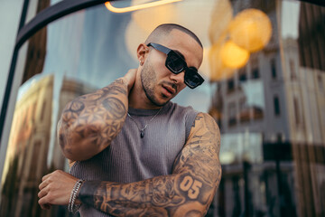 Hombre joven musculado y tatuado posando en la calle con ropa basica urbana 